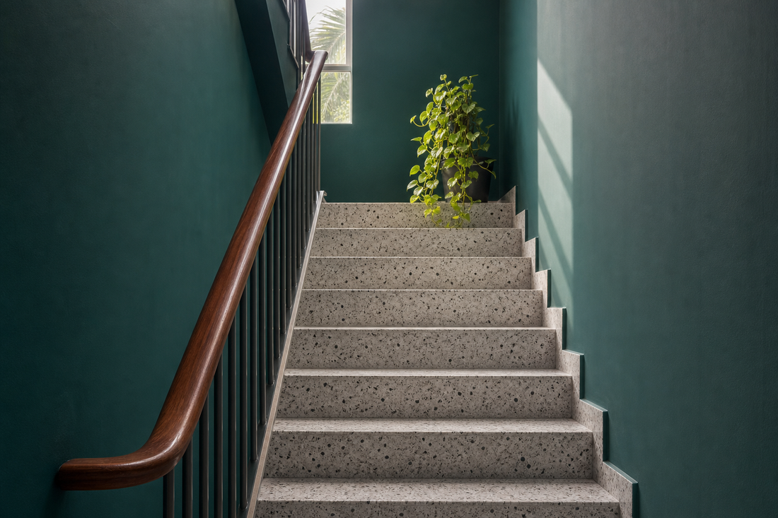 Link-house staircase with terrazzo steps and a wooden handrail by a deep teal wall, the kind of stairs where you might notice knee clicking